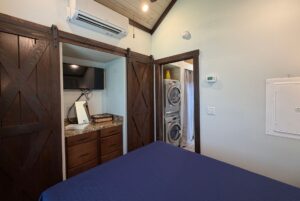 Bedroom at 59 Drifting Brook Lane features dark wood barn doors, TV, washer/dryer, and blue bedspread—ideal for real estate tours.