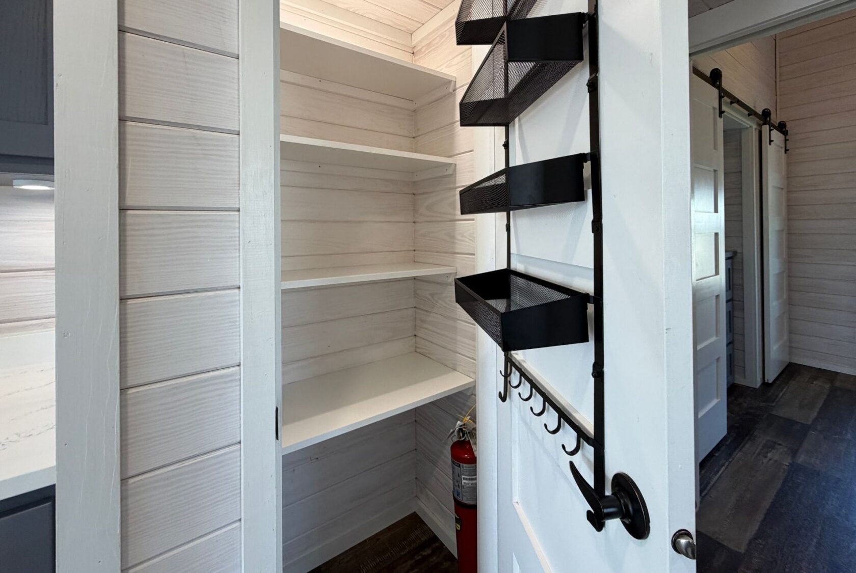 Small pantry with white shelves, black metal organizers, and a fire extinguisher—perfect for strolling Easy Lane.