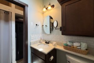Small bathroom at 59 Drifting Brook Lane features dark wood cabinets, round mirror, and white subway tile backsplash.