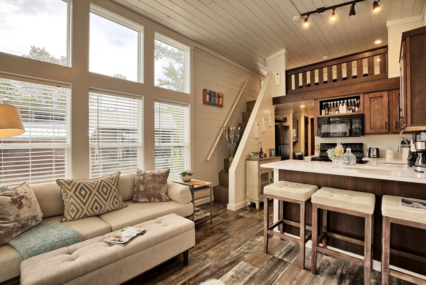 Cozy modern tiny house interior at 132 Drifting Brook with loft, kitchen, bar stools, sofa, and wood accents.