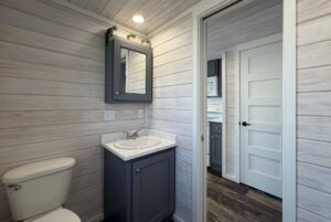 Small bathroom with gray vanity and wood panel walls, creating a Strolling Easy Lane vibe with sliding door and mirror cabinet.