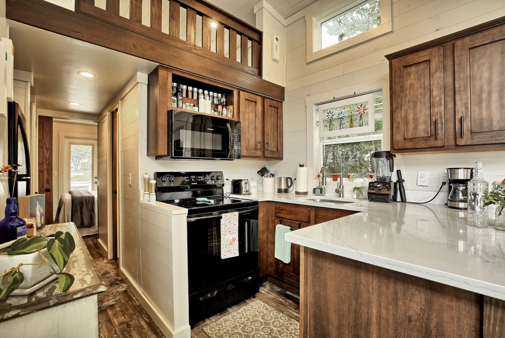 Tiny house kitchen at 132 Drifting Brook with wood cabinets, black appliances, and a cozy loft—perfect real estate find.