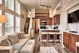 Modern tiny house interior at 132 Drifting Brook Lane with loft, cozy couch, kitchen, bar stools, and bright windows.