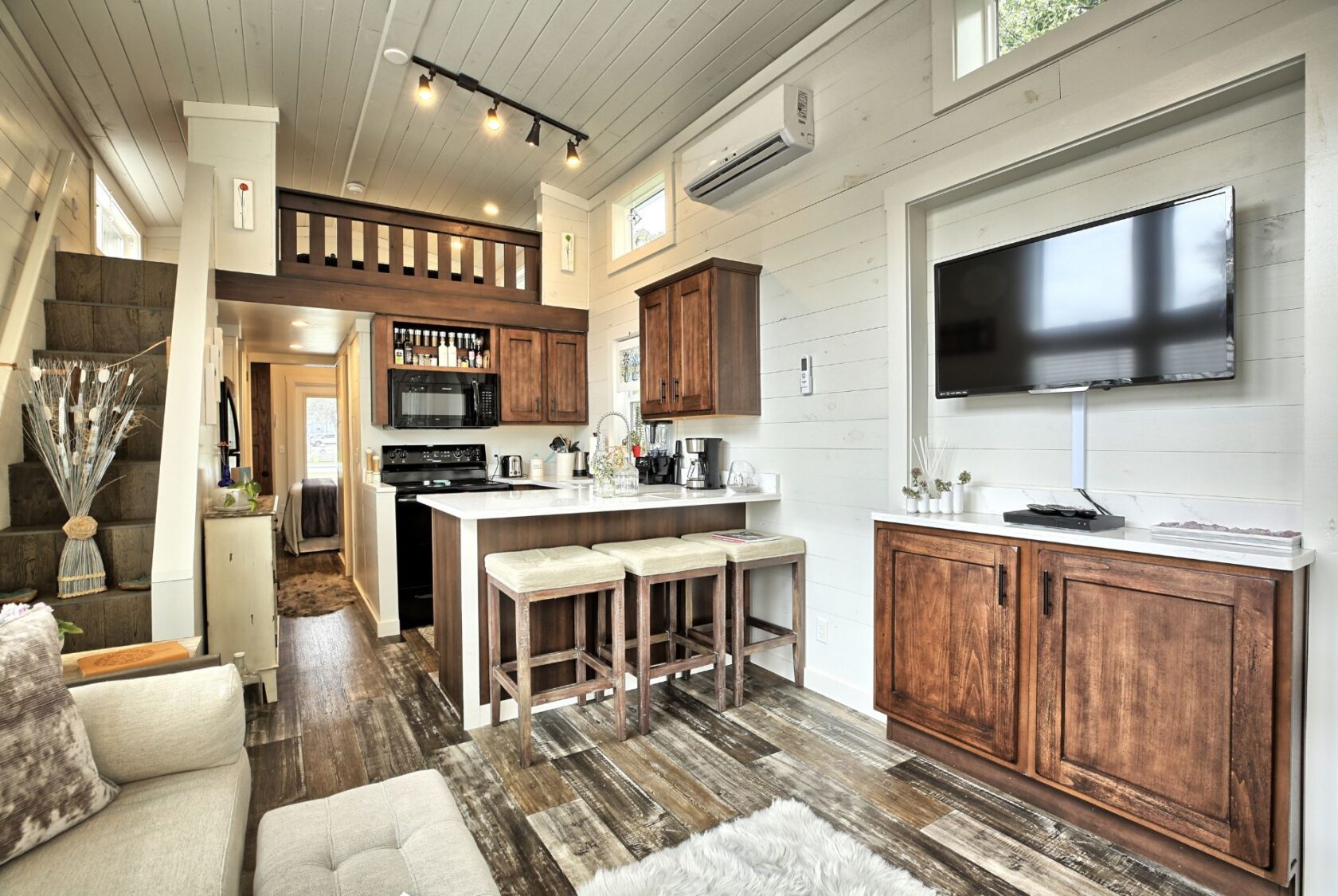 Bright, modern tiny home kitchen on Drifting Brook Lane with wood cabinets, loft, TV, and cozy breakfast bar for two.