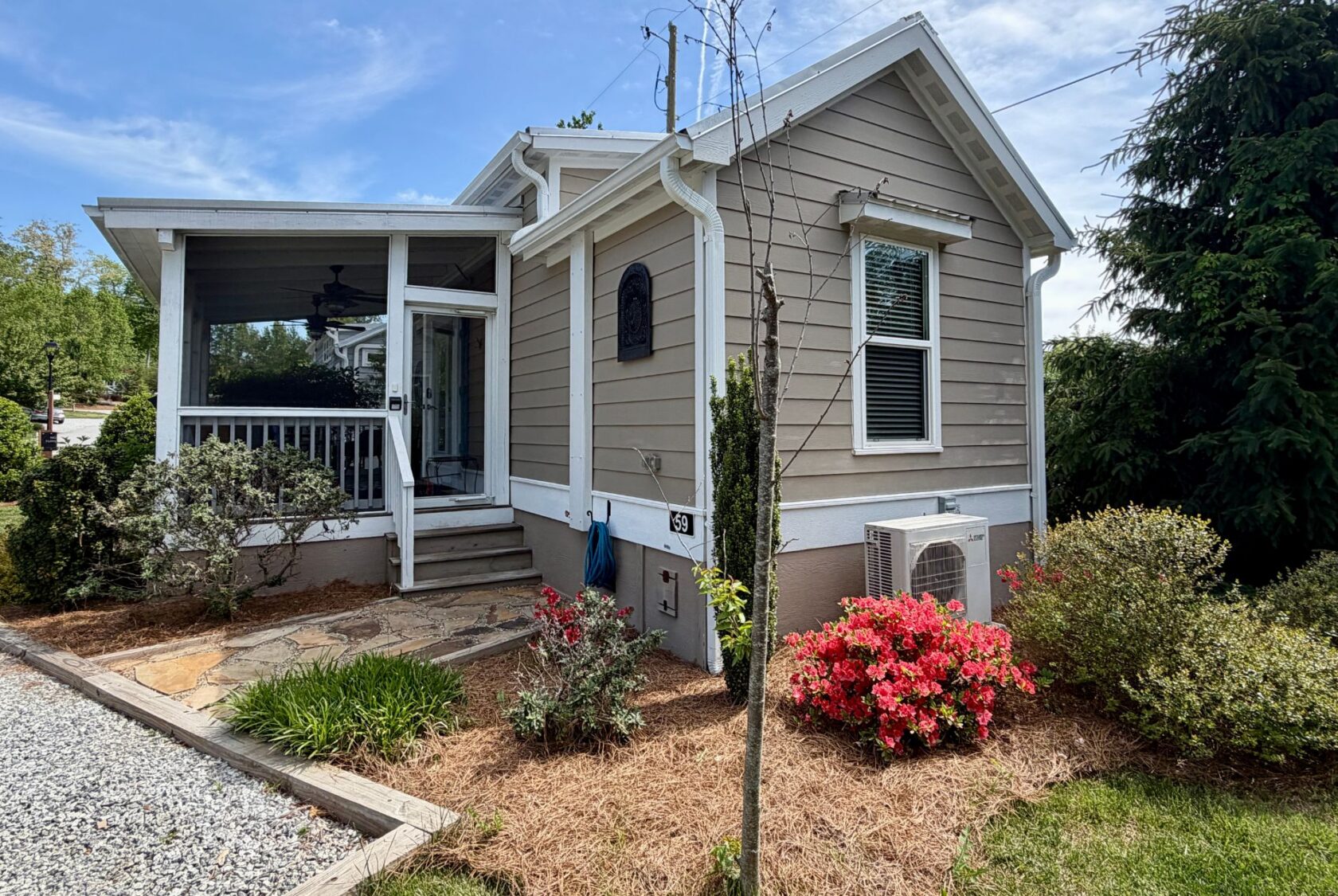 Charming beige house at 59 Drifting Brook Lane with screened porch, garden, red blooms, and gravel path under blue sky.