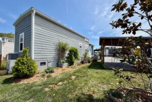 A small gray house with a garden on Easy Lane, carport nearby, and a sunny blue sky—perfect for strolling.