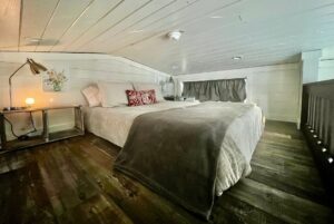 Cozy loft bedroom at 132 Drifting Brook Lane with a low ceiling, double bed, bedside lamp, and rustic wooden floors.