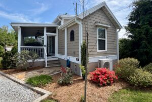 Charming beige house at 59 Drifting Brook Lane with screened porch, garden, red blooms, and gravel path under blue sky.