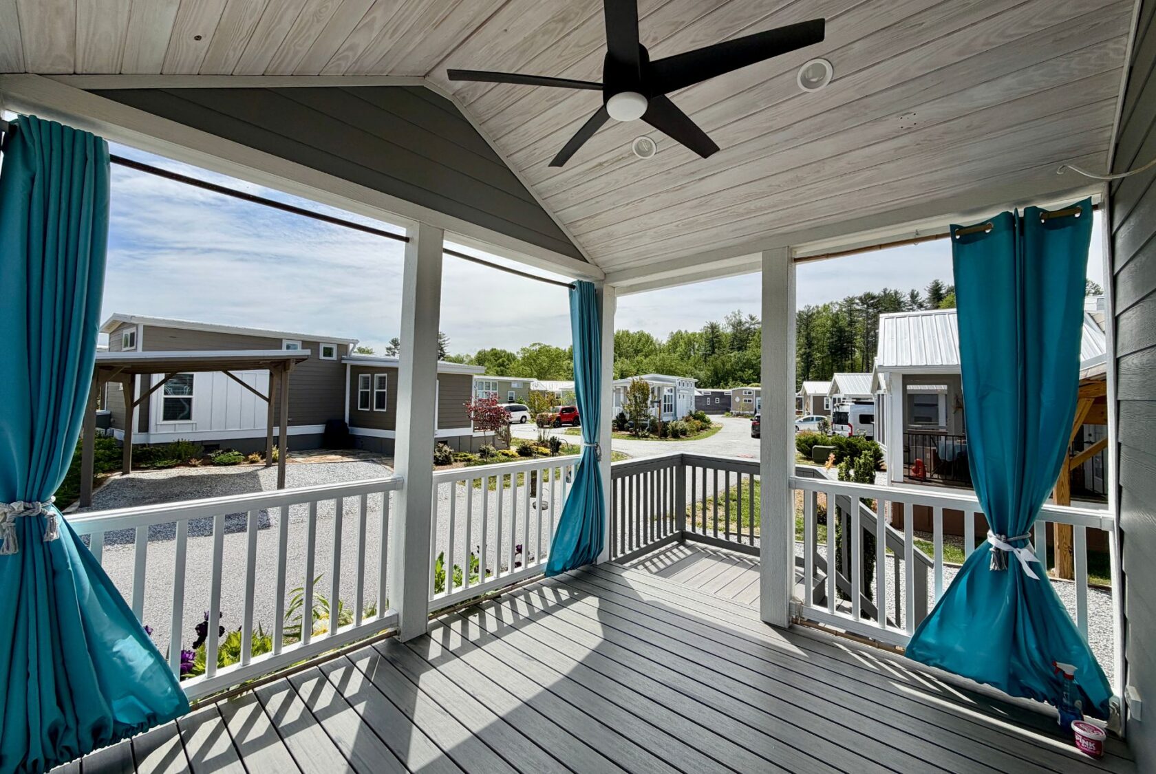 View from a covered porch with blue curtains, overlooking Strolling Easy Lane and a community of small modern homes.