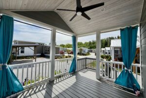 View from a covered porch with blue curtains, overlooking Strolling Easy Lane and a community of small modern homes.