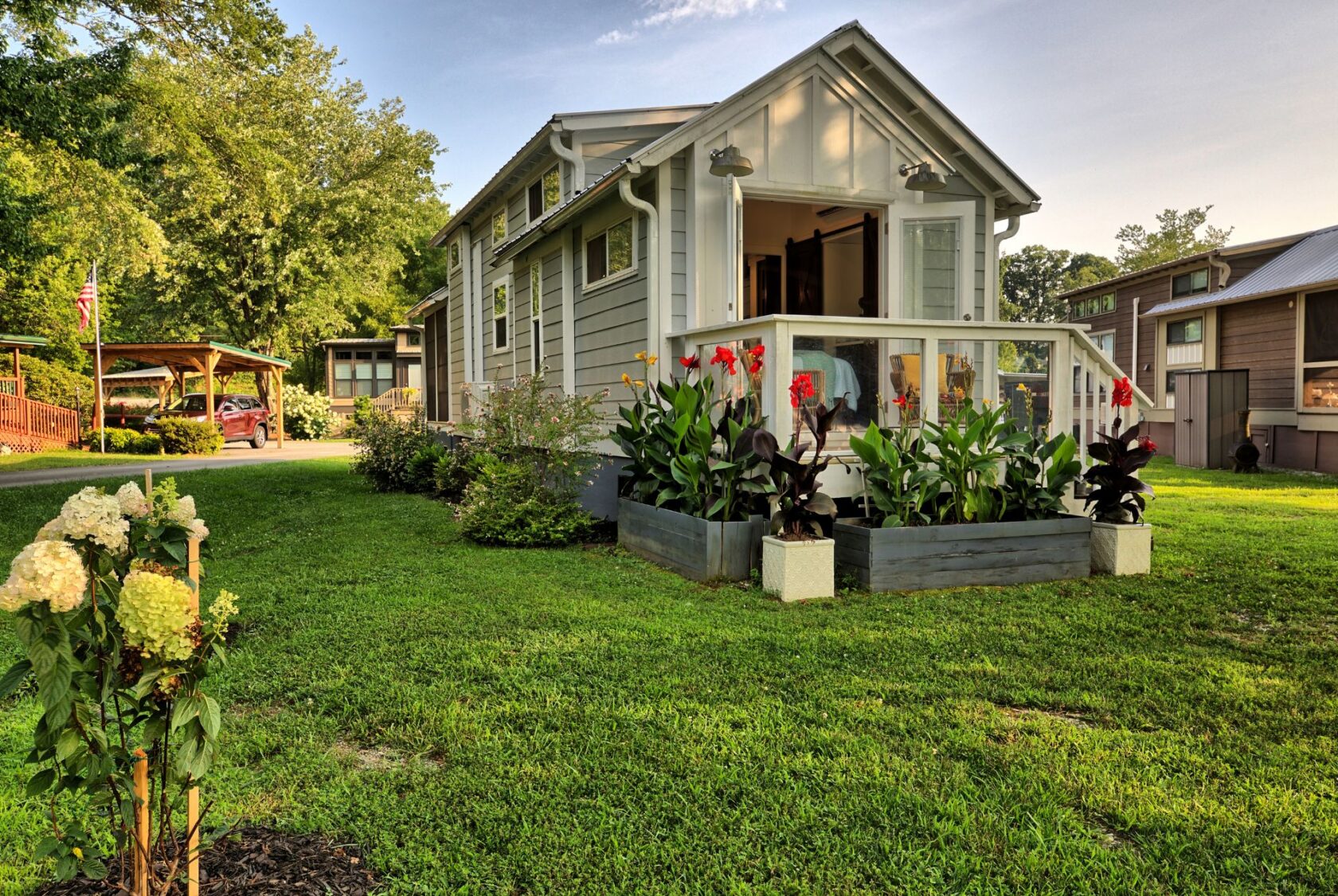 A small gray house with a porch at 132 Drifting Brook, surrounded by green lawn and colorful flower beds.