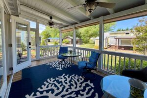 Screened porch with blue chairs and coral-patterned rug at 59 Drifting Brook Lane, overlooking a sunny neighborhood.