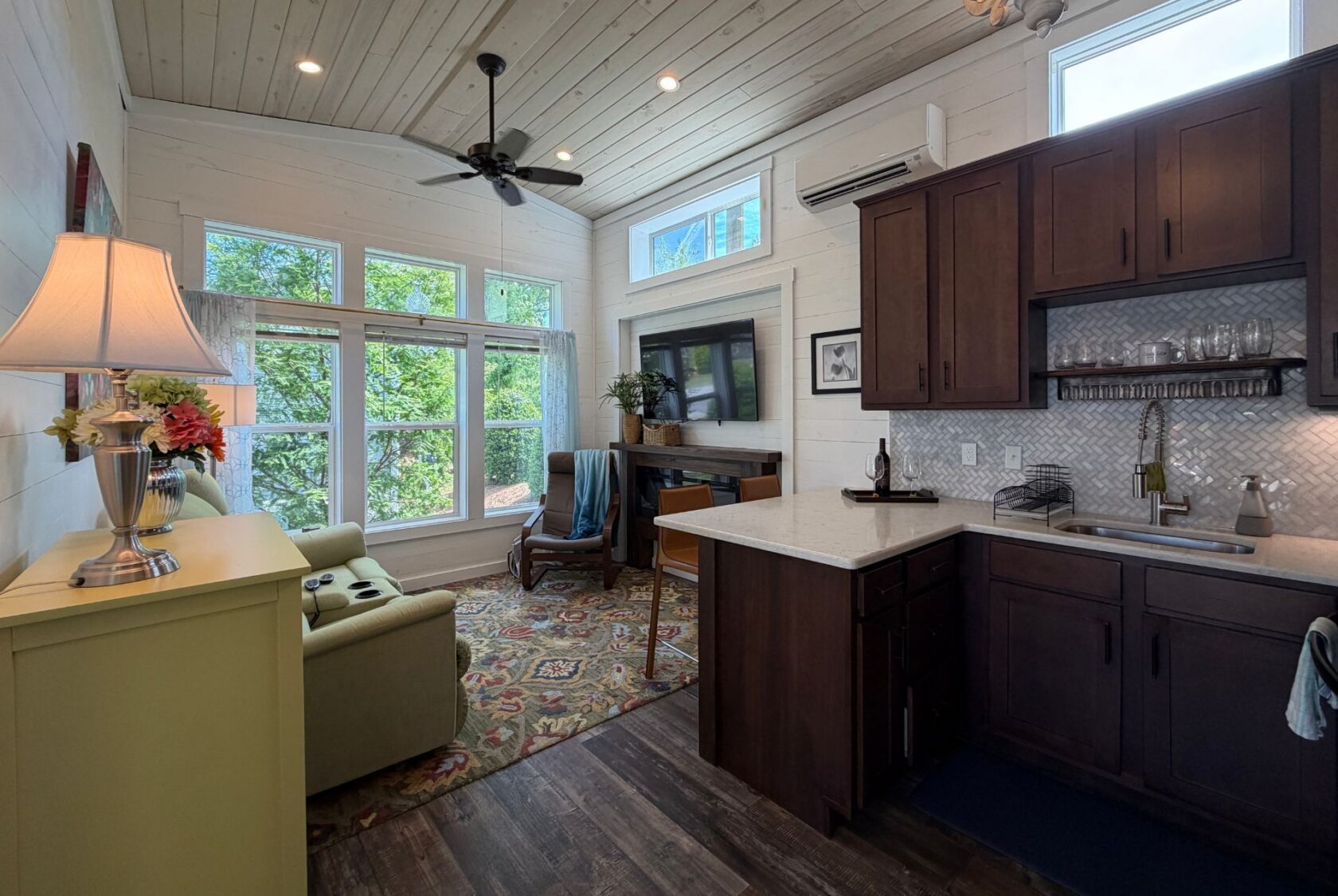 Cozy living room and kitchen at 59 Drifting Brook with large windows, dark cabinets, and a sofa facing the TV.
