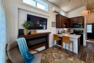 Modern tiny home kitchen and living area at 59 Drifting Brook with a TV, fireplace, bar stools, and cozy decor.
