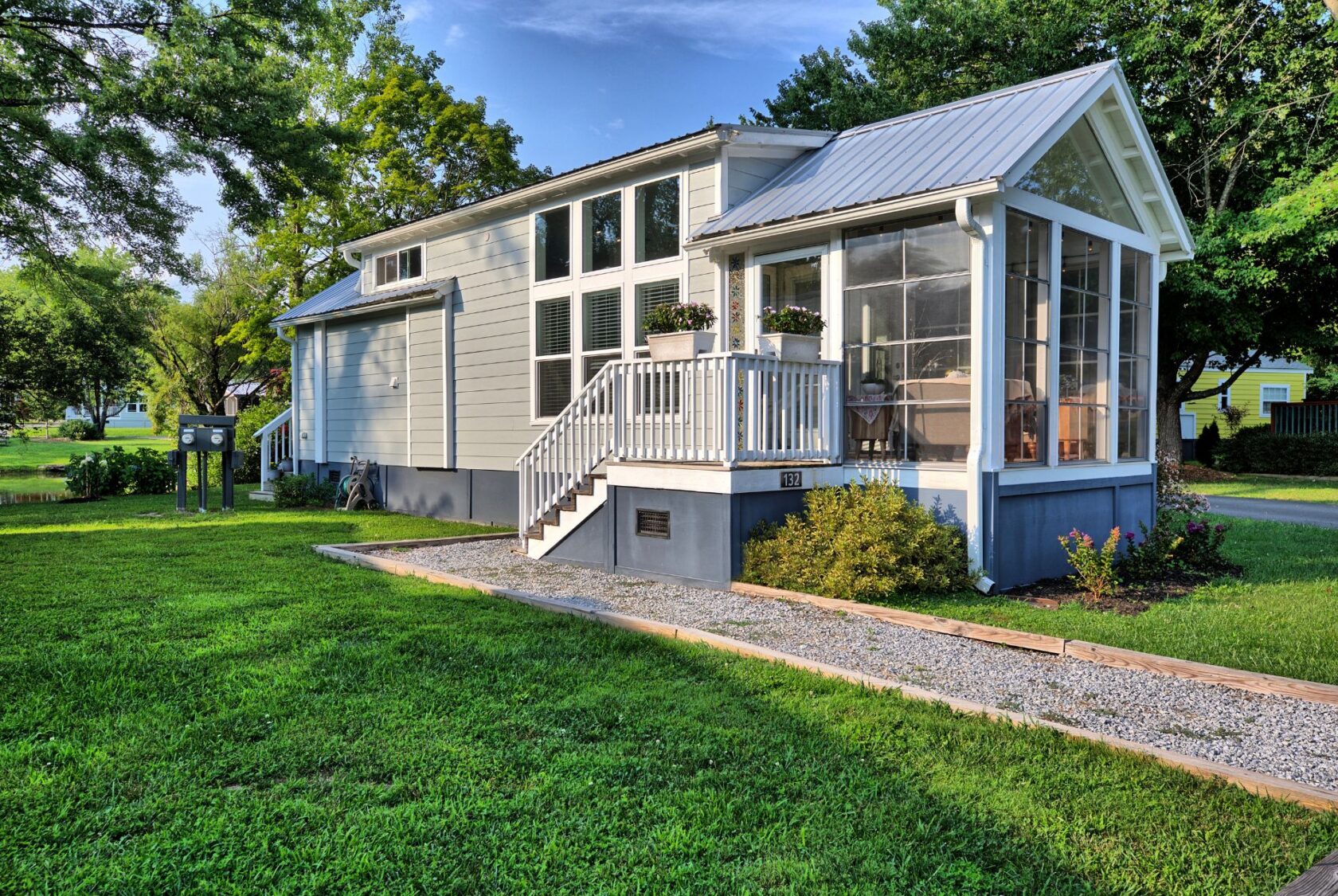 Small modern house with screened porch and white siding at 132 Drifting Brook, nestled among green grass and trees.