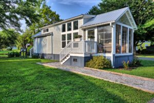 Small modern house with screened porch and white siding at 132 Drifting Brook, nestled among green grass and trees.