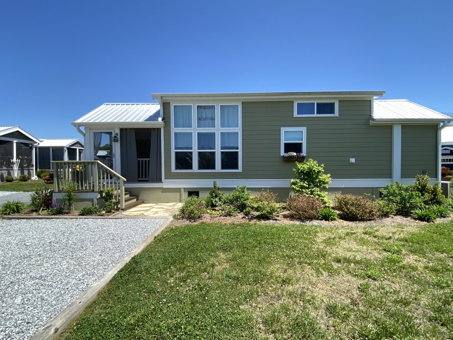 A small, modern green house on 43 Skipping Stone Lane with a porch and manicured lawn under a clear blue sky.