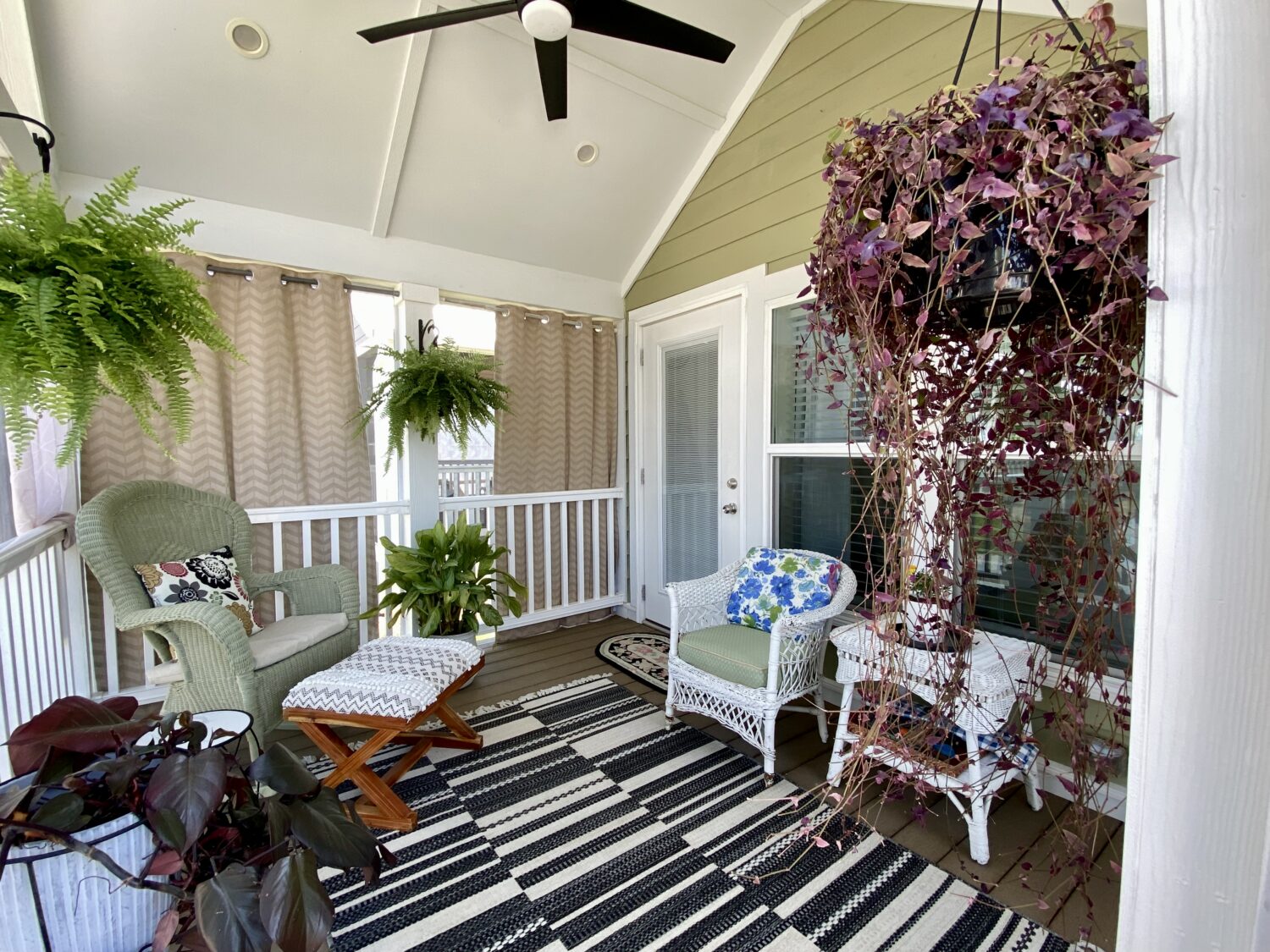 Cozy screened porch on Skipping Stone Lane with wicker chairs, potted plants, hanging ferns, and a striped rug.