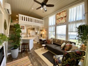 Cozy, sunlit tiny house on Skipping Stone Lane with a loft, modern kitchen, gray sofa, plants, and patterned decor.