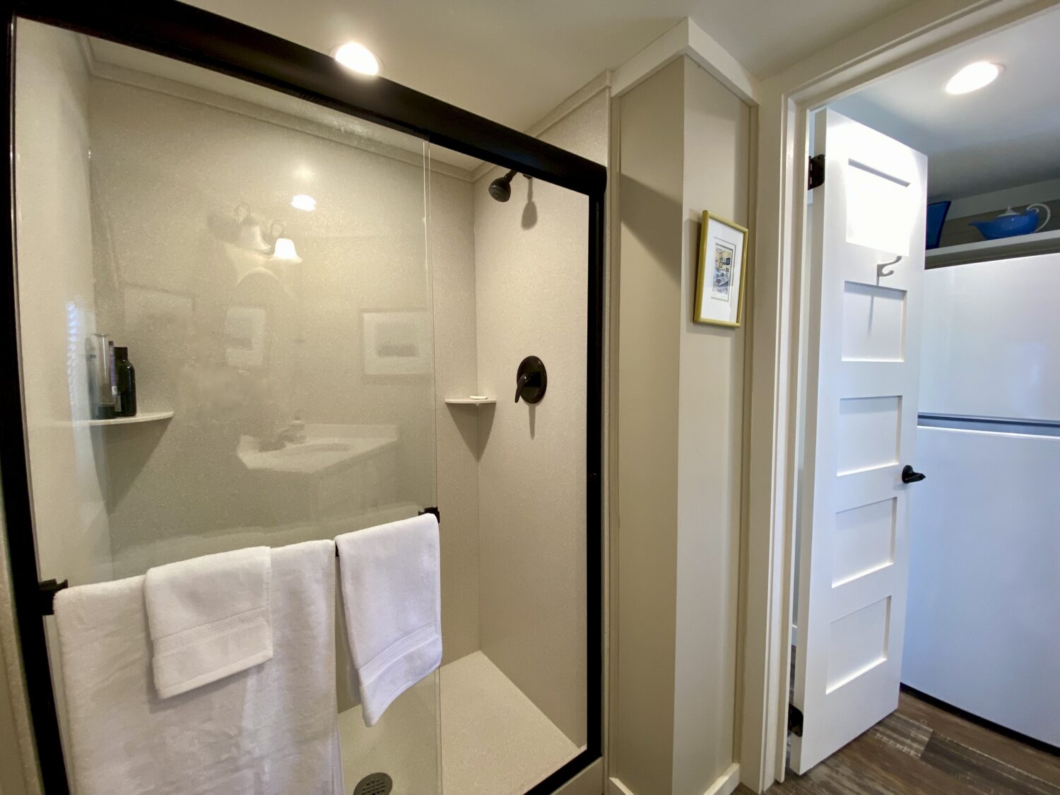 Bathroom at 43 Skipping Stone with a glass shower, white towels, and a view into a room with a white fridge.