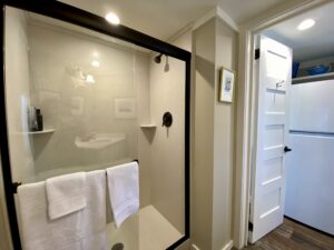 Bathroom at 43 Skipping Stone with a glass shower, white towels, and a view into a room with a white fridge.