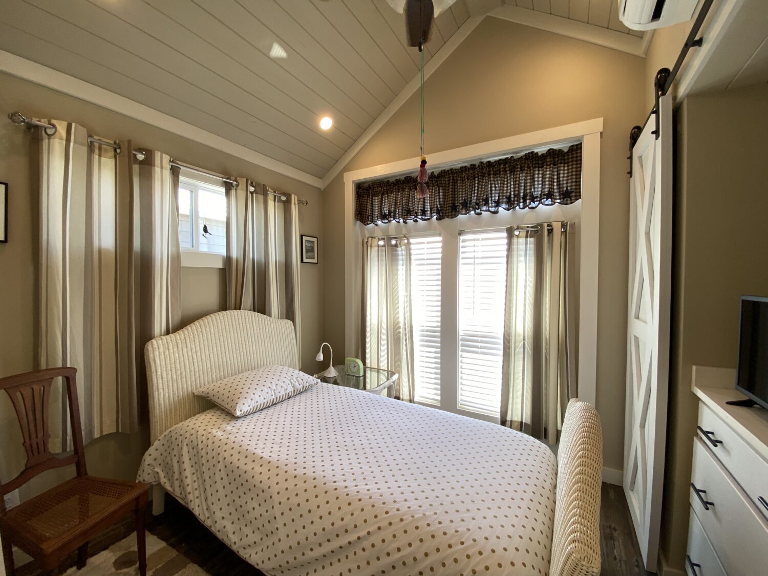 Cozy bedroom on Skipping Stone Lane with a single bed, wooden chair, dresser, and sunlit windows with curtains.