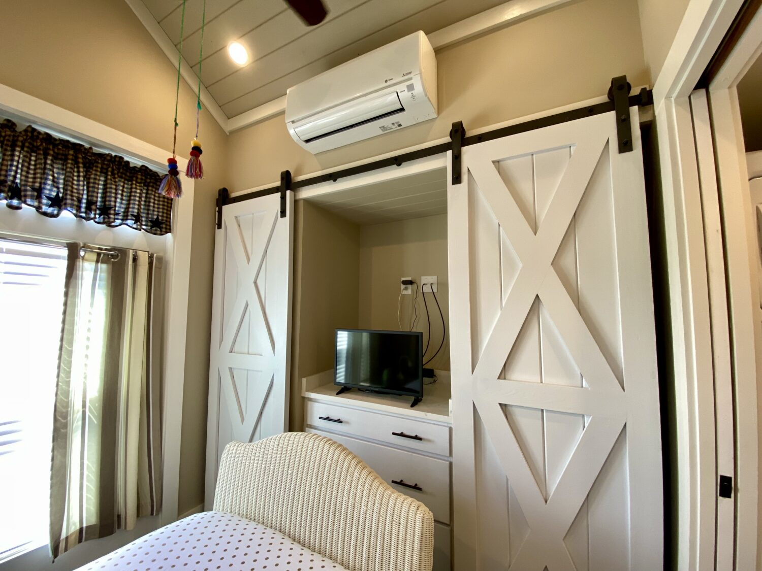 Cozy room on Skipping Stone Lane with barn-style closet doors, TV on dresser, and air conditioner above.