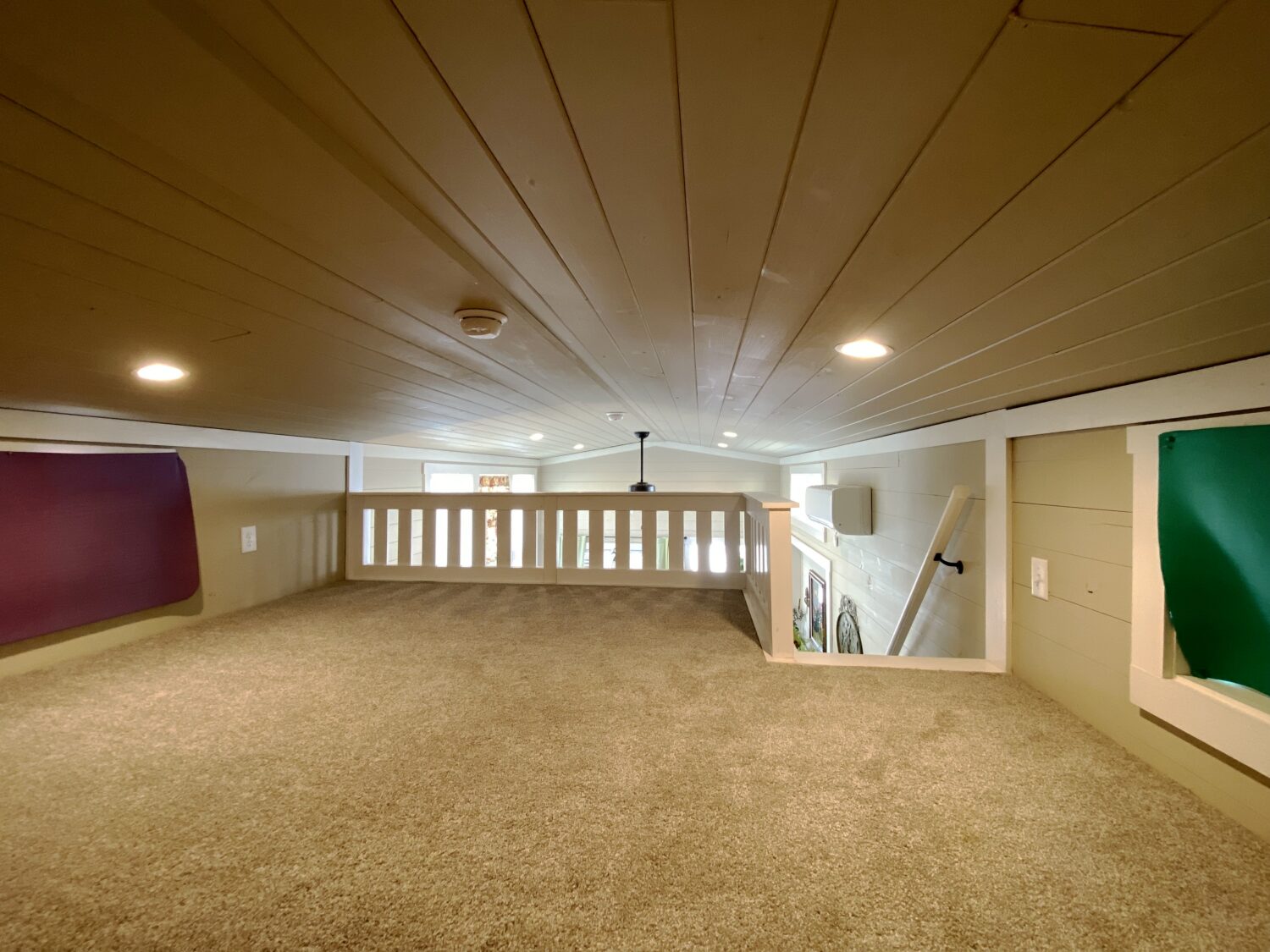 Low-ceiling loft area with carpeted floor and wood-paneled ceiling overlooks Skipping Stone Lane below.