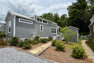 A modern tiny house with gray siding and a stone walkway on Mount Meadow Lane, set beneath a cloudy sky.