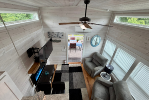 A modern, cozy living room on Mount Meadow Lane with large windows, gray furniture, and a door to the deck outside.