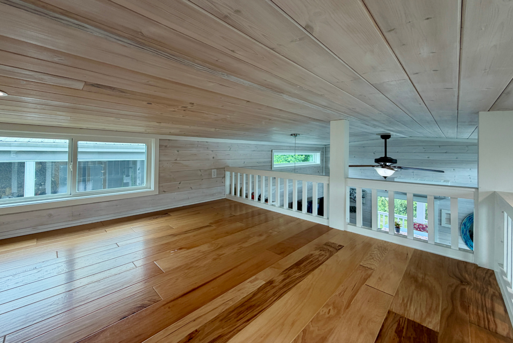 Loft with wood floors, white paneled walls and ceiling on Mount Meadow Lane, overlooking a room with large windows.
