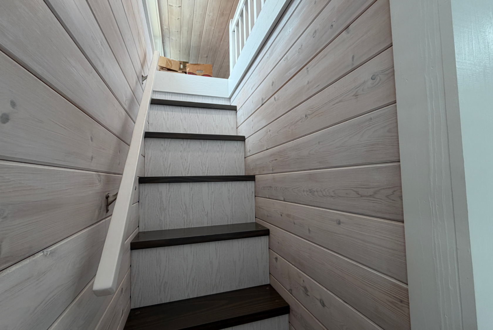 Wood-paneled staircase with a handrail, leading up to a landing with cardboard boxes on Mount Meadow Lane.