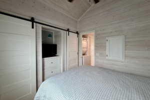 Cozy bedroom on Mount Meadow Lane with white paneled walls, patterned bedspread, TV, and sliding doors to laundry area.