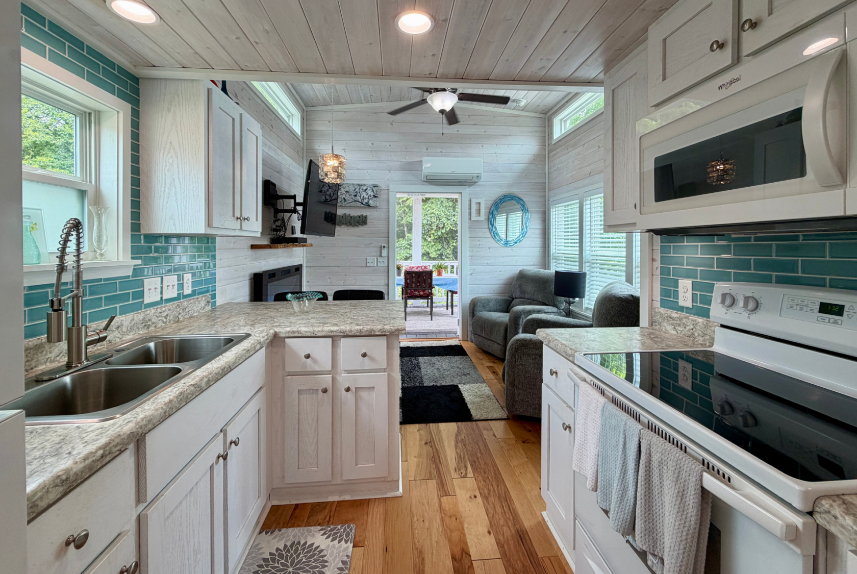 Tiny house interior on Mount Meadow Lane with modern kitchen, teal backsplash, living area, and large windows for natural light.