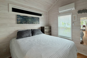 A cozy Mount Meadow Lane bedroom features gray bedding, a dresser, blinds, and a Monet-style painting on the wall.