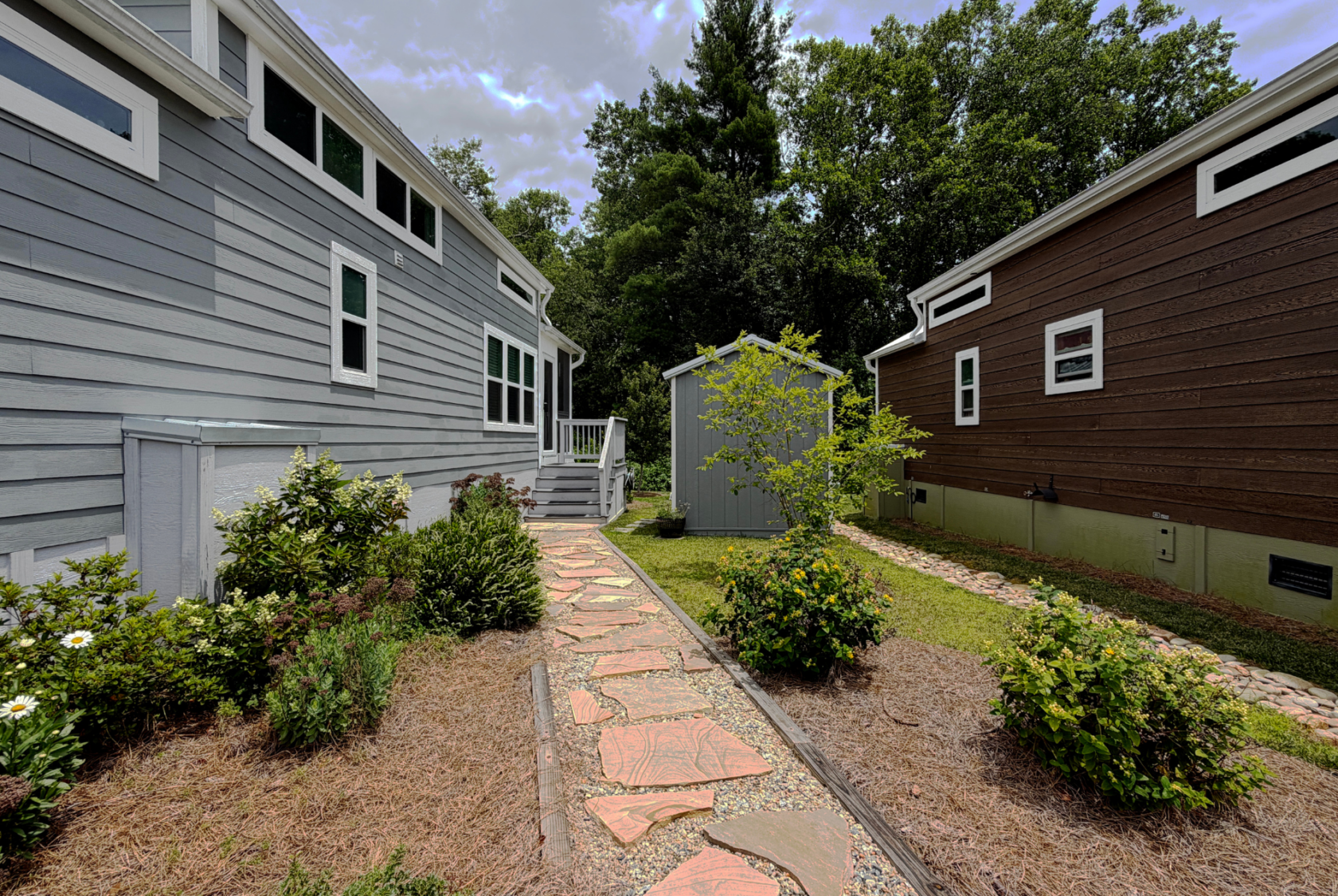 Stone path on Mount Meadow Lane between two small houses, surrounded by bushes and trees under a partly cloudy sky.