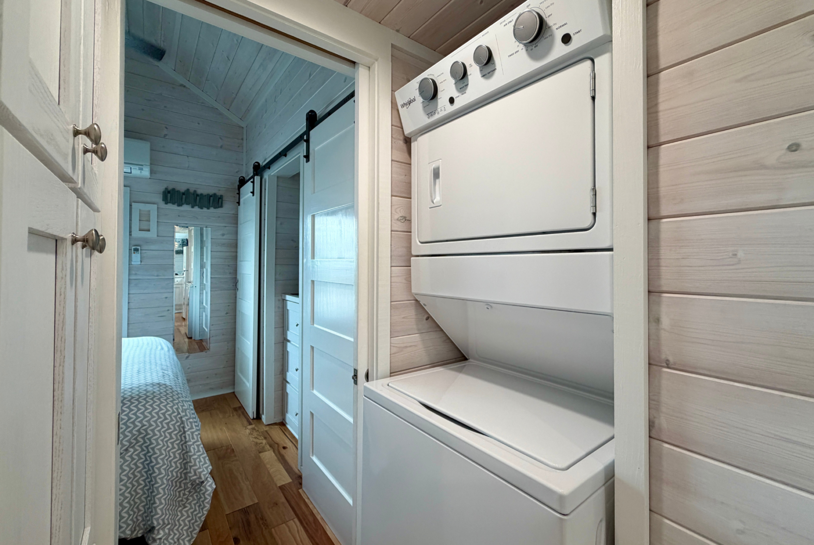 Stacked washer and dryer unit in a hallway with wood panel walls on Mount Meadow Lane, near a cozy bedroom.