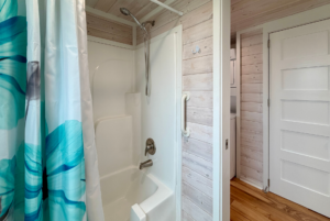 White bathtub and shower with teal curtain, grab bar, and wood-paneled walls on Mount Meadow Lane near laundry area and door.