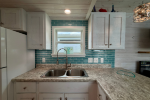 A Mount Meadow Lane kitchen with white cabinets, teal subway tile backsplash, and a double sink under a window.