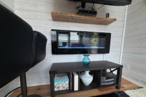 Electric fireplace with blue flames on a white wall at Mount Meadow Lane, black chair, and dark table with decor below.