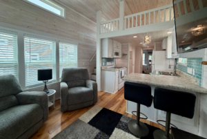Cozy tiny house interior at 74 Mount Meadow Lane with gray armchairs, loft, modern kitchen, and marble counter bar stools.