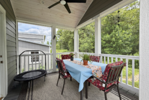 Screened porch on Mount Meadow Lane with a dining table, four chairs, potted plants, and mini trampoline overlooking greenery.