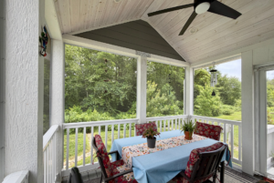 Screened porch on Mount Meadow Lane with a table, chairs, potted plants, and a ceiling fan, overlooking green trees.