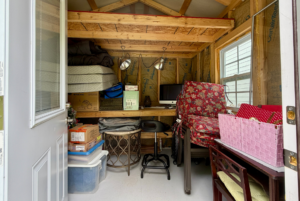 Small, cluttered shed office on Mount Meadow Lane with a desk, stacked boxes, lamps, and stored household items.