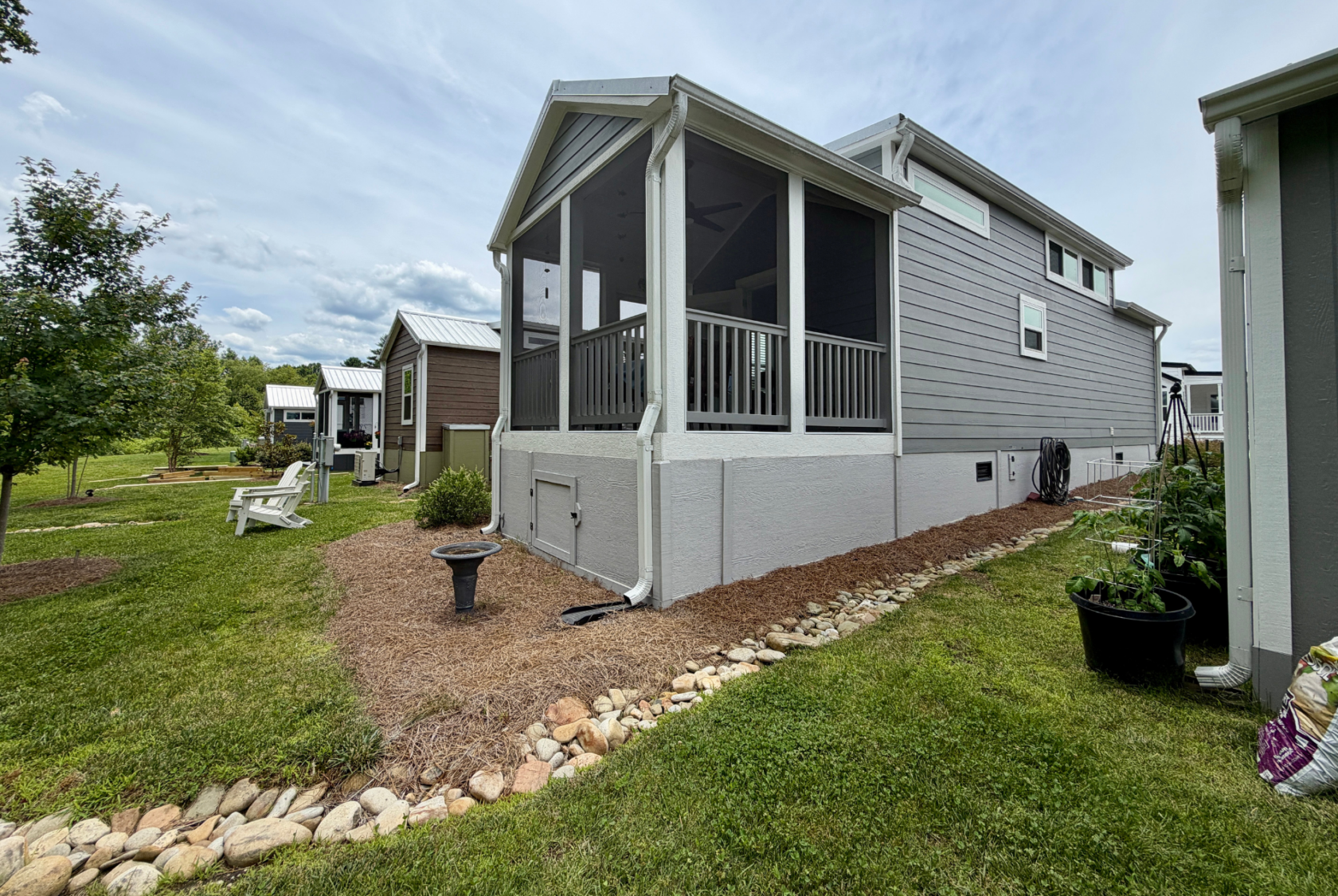 Gray house on Mount Meadow Lane with a screened porch, garden beds, and lawn chairs in a grassy, tree-lined backyard.