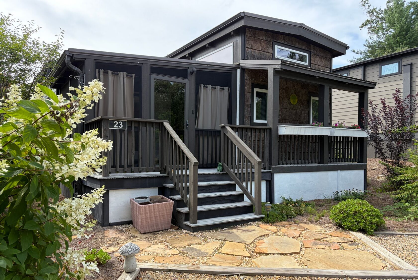 Small modern cottage on Highland Hill Lane with a screened porch, wooden steps, plants, and a stone entrance path.