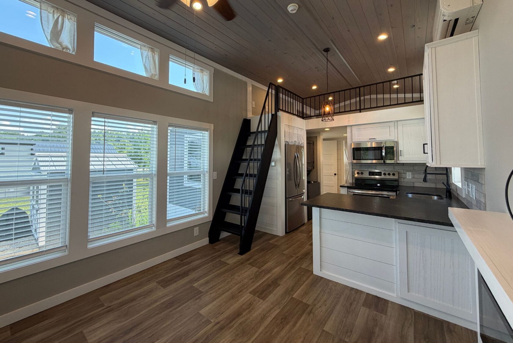Modern tiny house kitchen at 103 Meandering Lane with white cabinets, wood floors, and airy loft stairs.