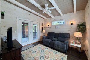 Cozy living room on Highland Hill Lane with recliner, rug, TV, lamps, ceiling fan, and French doors to a screened porch.