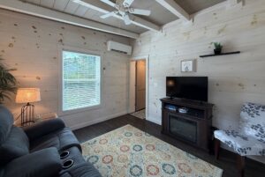 Cozy living room at 23 Highland Hill with TV, recliner, patterned rug, window blinds, and light wood paneling throughout.