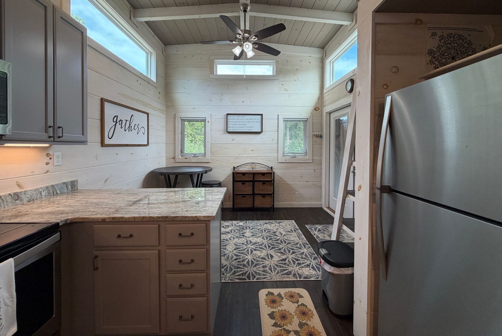 Tiny house kitchen on Highland Hill Lane with stainless appliances, light wood walls, and a dining nook by two windows.